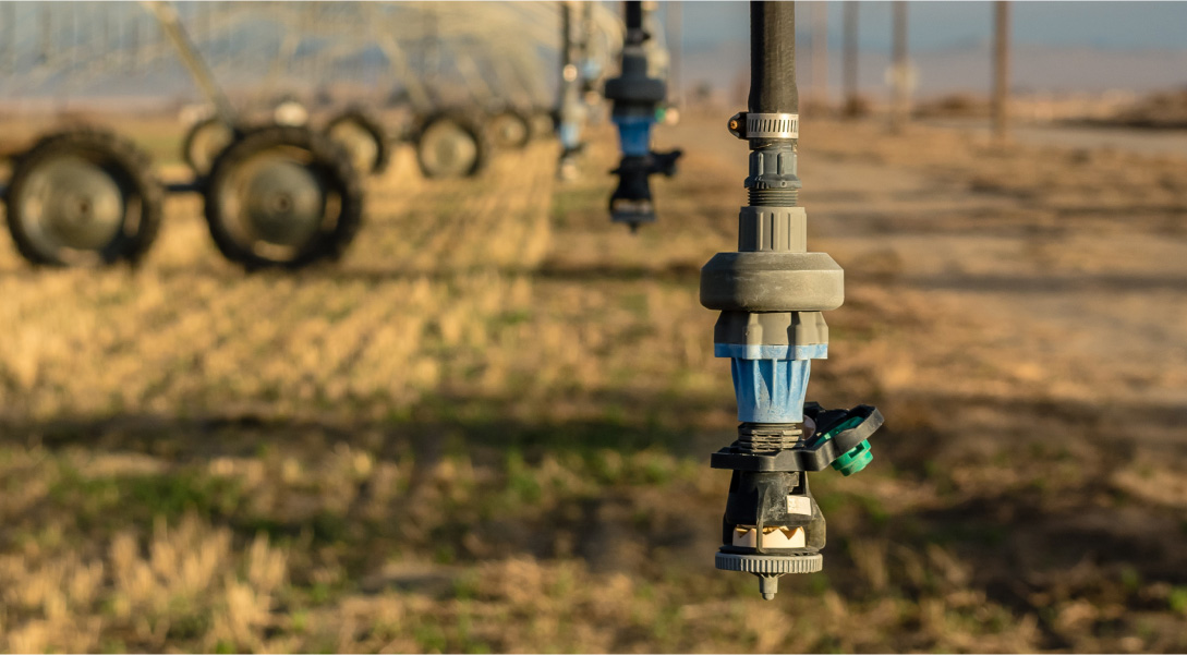 sprinkler nozzle in dry field with tractors in background